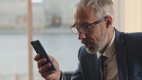 Close up portrait of mature businessman using smartphone apps. Handsome senior executive in eyeglasses and suit texting message on mobile phone over blurred background Stockvideo