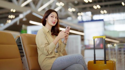 Asian woman waiting for departure at the airport on vacation holiday. Asia female passenger using mobile smart phone and sitting in terminal hall while waiting for her flight Arkivvideo
