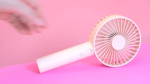 Female hand turns on a mini fan on pink background close-up, side view. 库存视频
