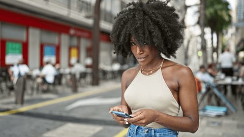 African american woman using smartphone smiling at street: stockvideo