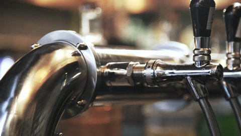 Pan shot of shining beer taps in a bar. Blurred background with a person walking. Left to right pan slow motion close up shotの動画素材