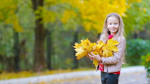 Adorable little girl with yellow maple leaves outdoors at beautiful autumn parkの動画素材
