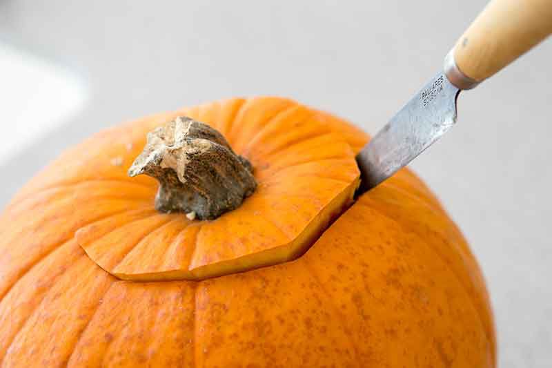 A knife cutting the top off of a pumpkin 