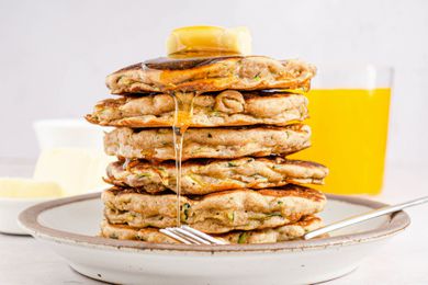 A tall stack of sweet zucchini pancakes on a plate with butter and syrup on top
