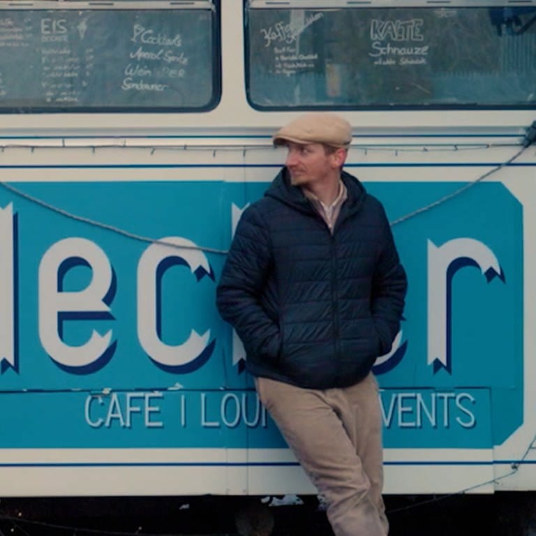 Junger Mann mit Mütze lehnt an altem Bus