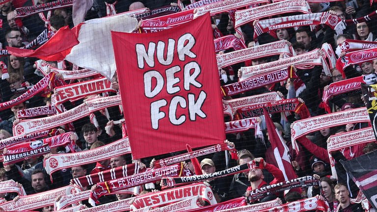 FCK-Fans halten im Stadion Schals hoch und eine Fahne mit der Aufschrift „Nur der FCK“.