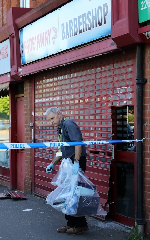 A detective removes items from a barbers shop in Moss Side