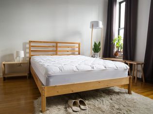 Leisure Town Mattress Pad displayed on wood bed with nearby faux fur area rug, nightstand, lamps, and brown draperies