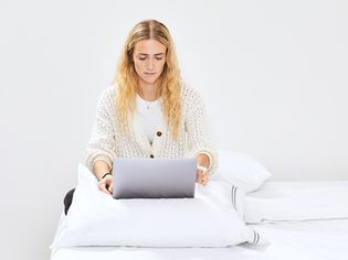 Person sitting on a bed made with Frette Hotel Classic sheet set while working on a laptop