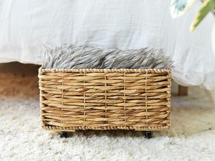 Small basket with small wheels used under the bed storage on white rug