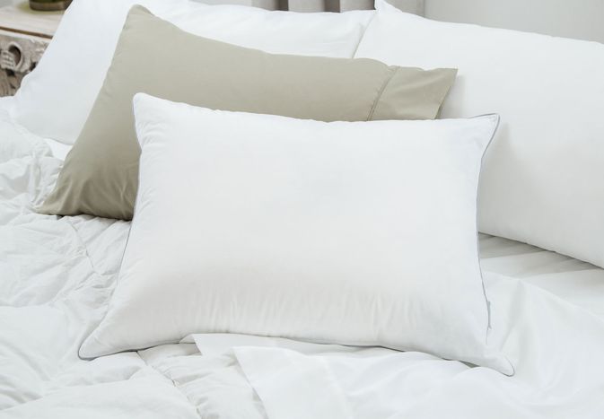 Tuft & Needle down pillow displayed on a bed with white sheets and a brown pillow