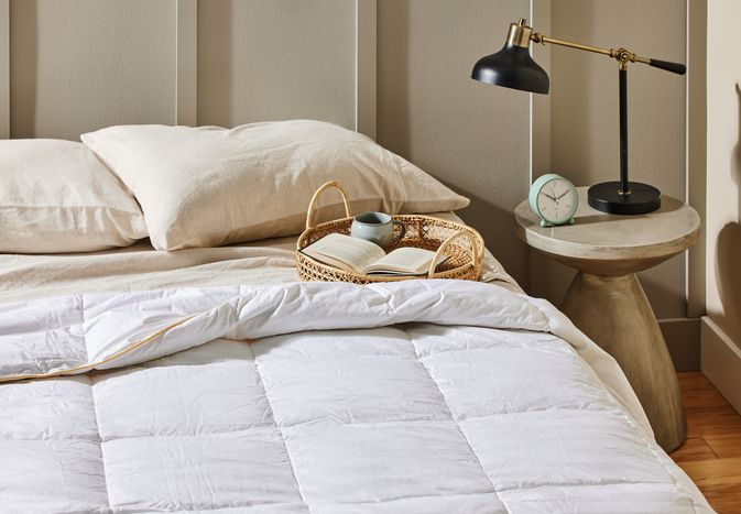 A bed near a nightstand adorned with the Alwyn Home All Season Goose Down Comforter