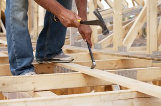 close-up of construction worker balancing on wood frame house working with hammering tools