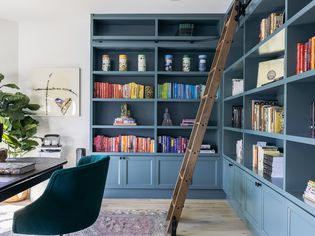 Large blue bookcase with books organized by color with ladder in front
