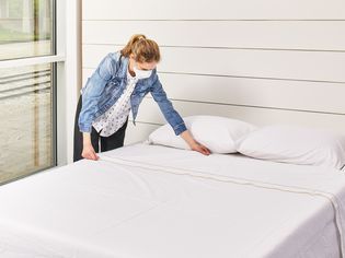 Person wearing mask making bed with the Kassatex Salerno Percale Sheet Set