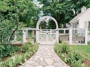 A front yard garden with a wood-framed hog wire fence and a matching arched gate