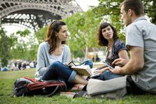 Group of people talking as they sit under the Eiffel Tower.