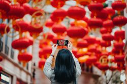 Rear view of woman taking photos of traditional Chinese red lanterns with smartphone on city street