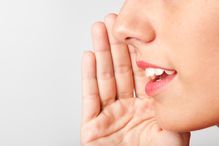 Close up of woman's mouth and nose with hand up as if whispering