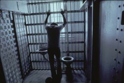 Man in jail cell with arms on bars