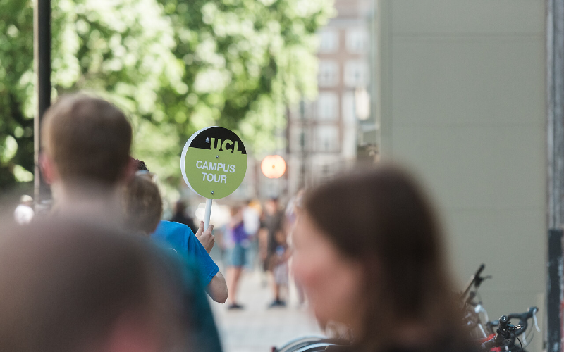 A student ambassador holds up a green sign that says "UCL campus tour".