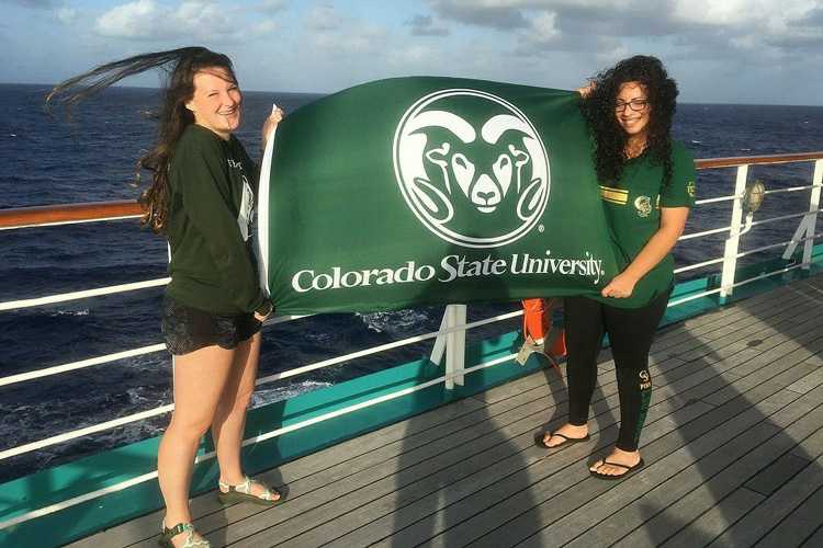 Two students hold a CSU flag on a ship out at sea
