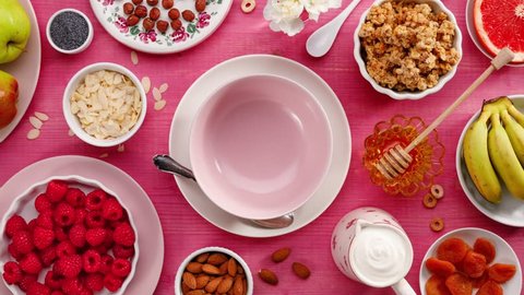 Granola with natural yogurt, fresh raspberries, honey, almond flakes and poppy seeds in a ceramic bowl on a pink wooden table, top view. Healthy eating concept, perfect breakfast or dessert. : vidéo de stock