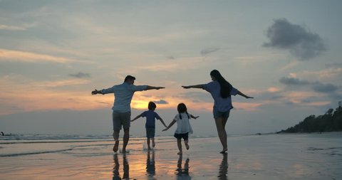 Silhouetted happy asian family playing and having fun on the beach at sunset. Slow Motion. Family, Freedom and Travel concept. - Βίντεο στοκ