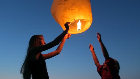 Two young girls launching a Chinese sky fly fire lantern to make a wish, summer holidays, celebration, family, children 스톡 비디오