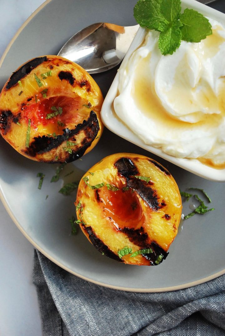 grilled peaches on a gray plate with yogurt and a spoon