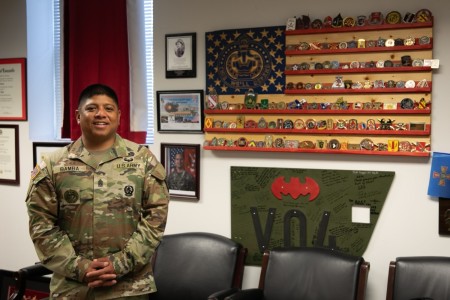 Command Sgt. Maj. John Bamba stands in front of his military coin collection. Bamba received the coins from several military and organizational leaders over his 26-year military career.