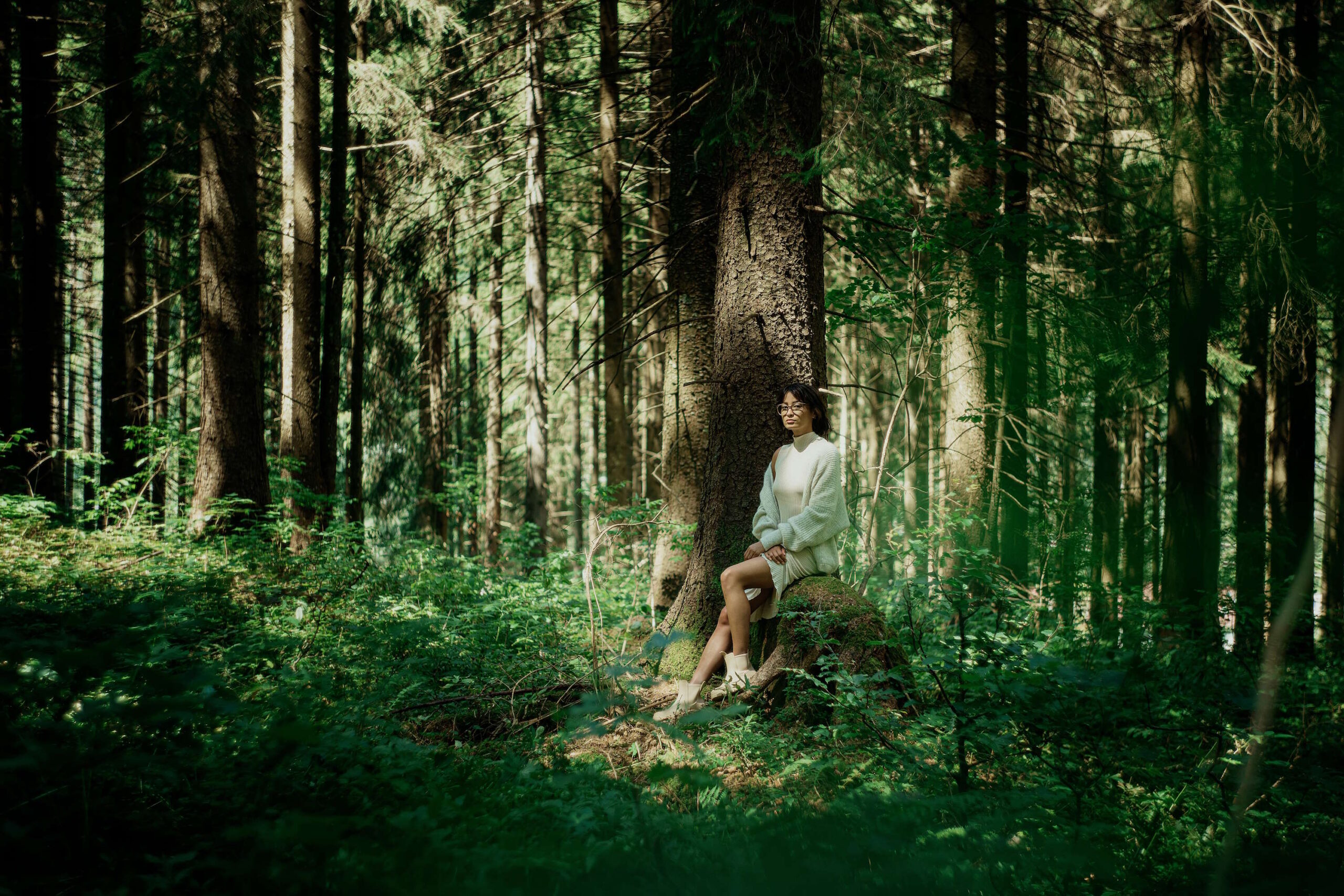 Frau sitzt im Wald an einem Baum