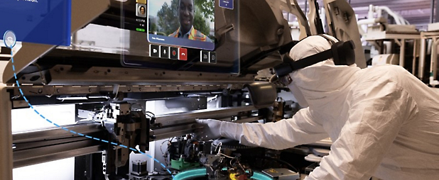 A technician in a cleanroom suit operates advanced manufacturing equipment in a high-tech facility.
