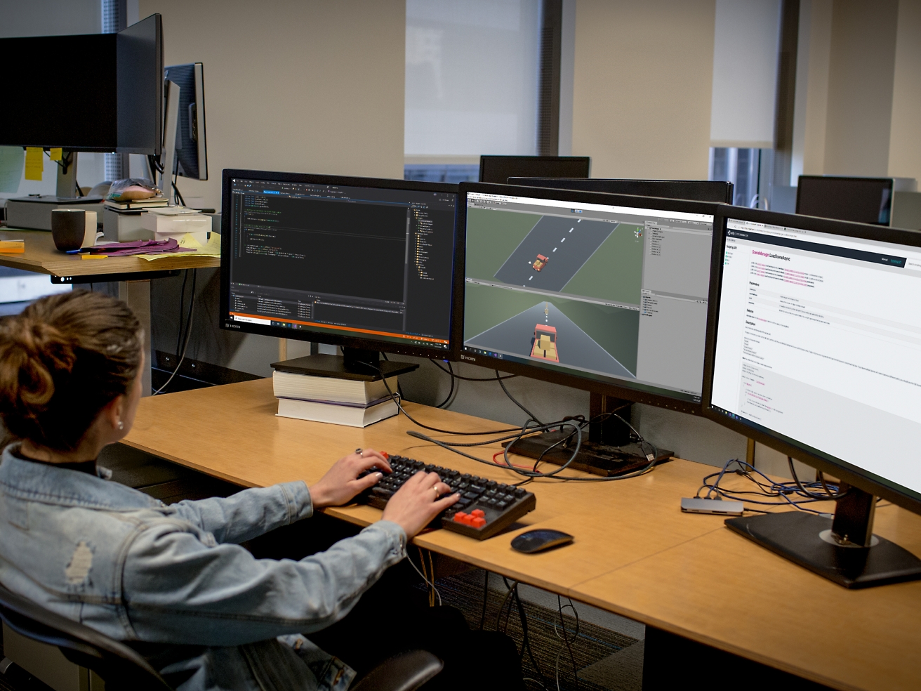 A female software developer working at a multi-monitor setup in an office, coding and debugging software.