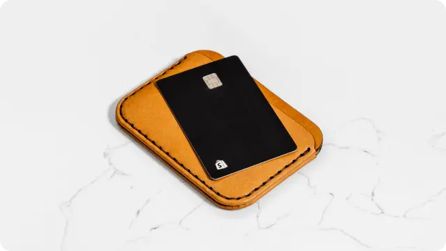 A leather wallet and black Shopify Balance card sit on a white surface.