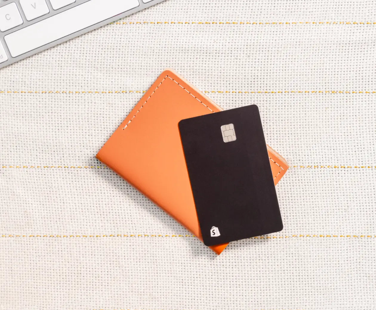 A leather wallet and black Shopify Balance card sit on a striped desk.