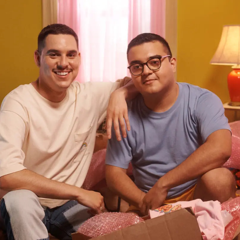 Two men wearing t-shirts and smiling sit in a room with yellow walls.