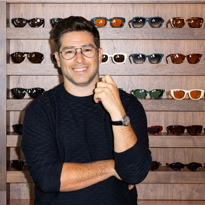 Gary Black, Founder and President of Black Optical, smiles in front of a wall of trendy sunglasses