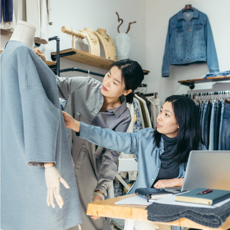 Deux femmes dans une boutique, touchant une veste sur un mannequin, avec des jeans et des vestes en jean à l’arrière-plan.