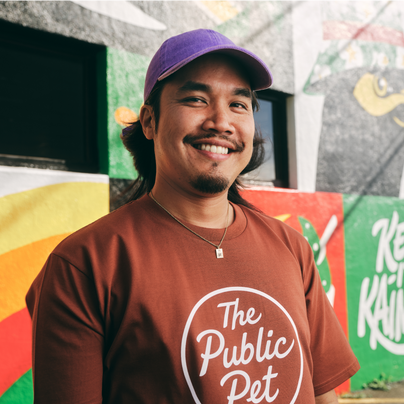 Jordan Lee, Owner of The Public Pet, smiling proudly in front of an outdoor mural and modeling a The Public Pet t-shirt