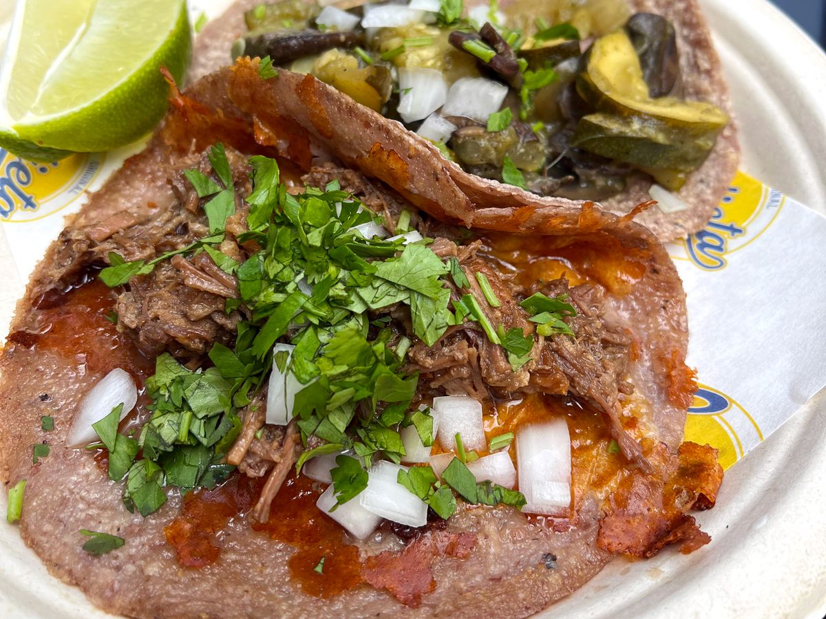 A closeup on a suadero taco, with a second taco and lime wedges beyond.