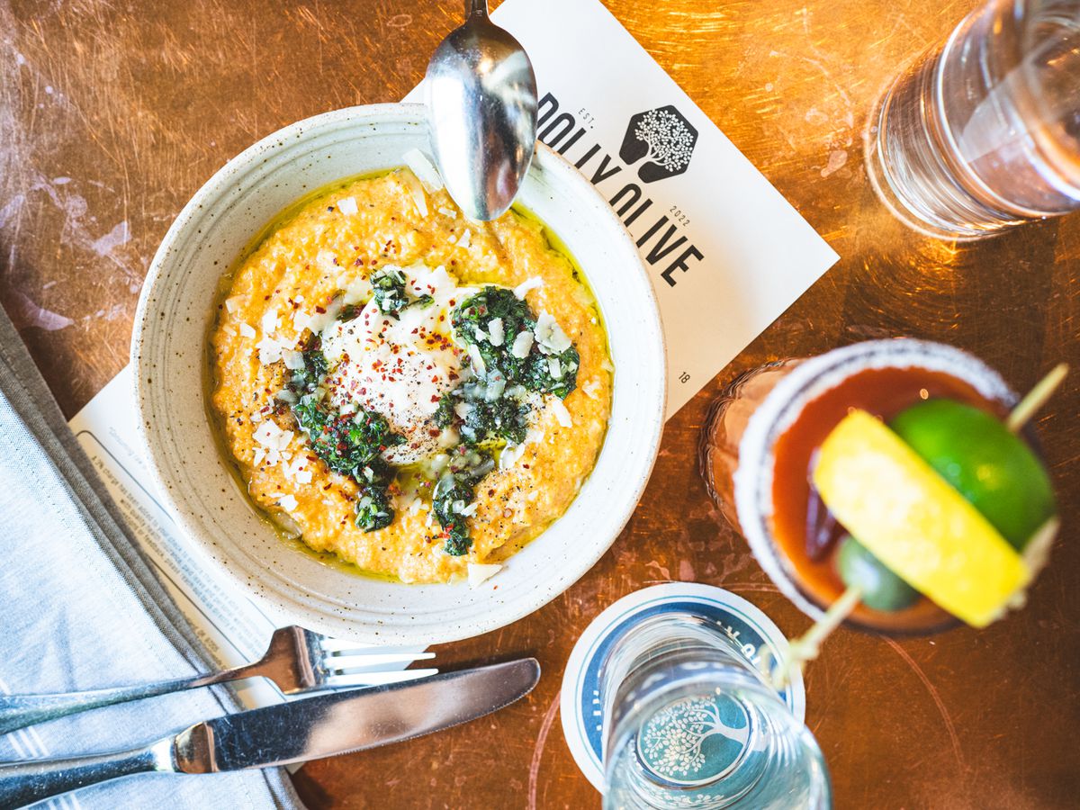A bowl of polenta at Dolly Olive with an egg. It sits on a table next to a bloody mary.