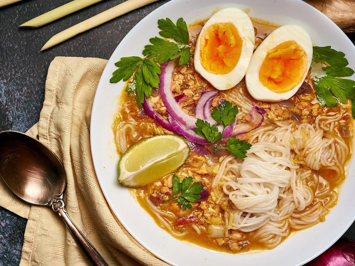 A bowl of noodles with boiled egg, cilantro, onion, and lime.