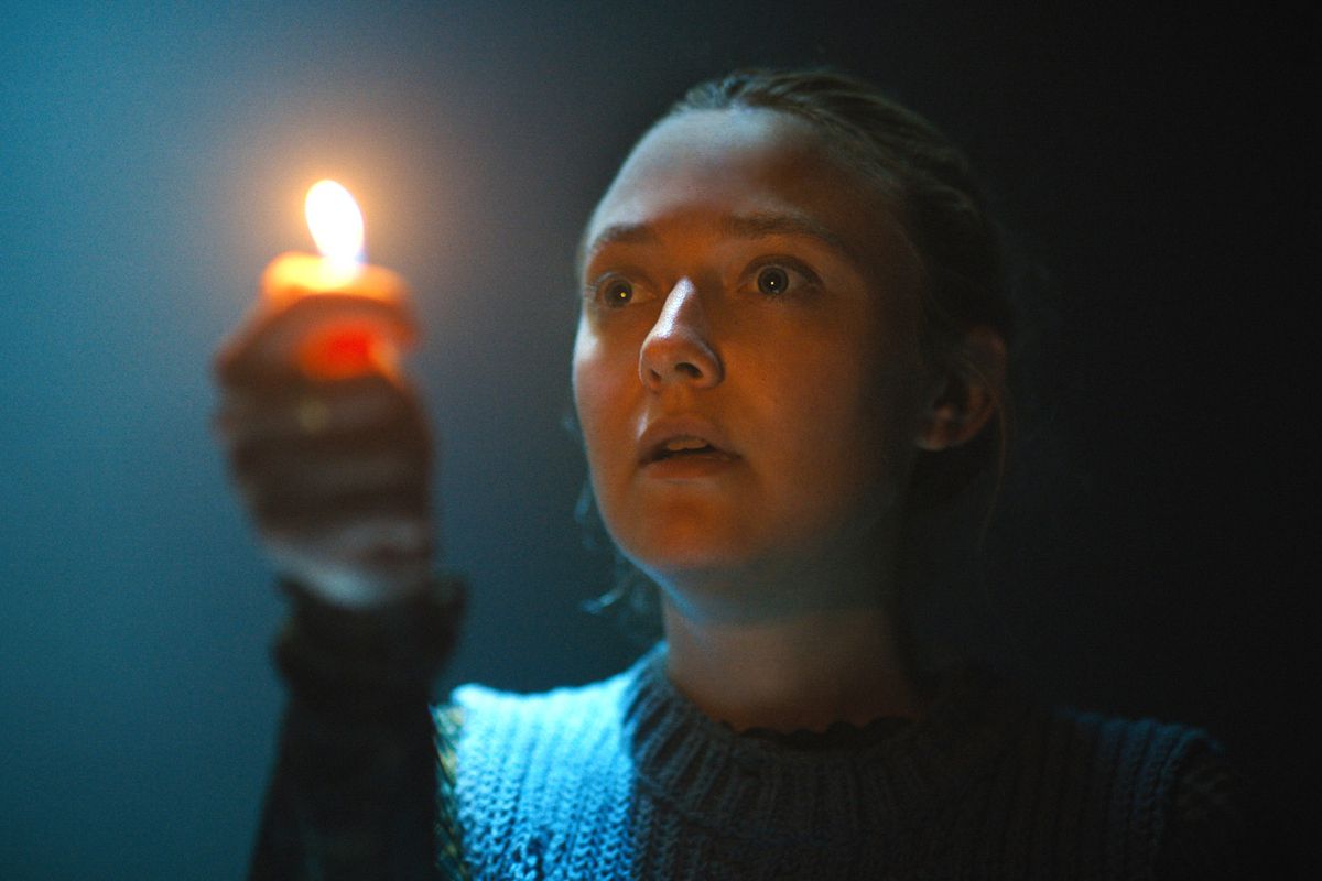 Mina (Dakota Fanning) holds up a lighter with the flame lighting her face as she explores a dark cavern in Ishana Night Shyamalan’s The Watchers