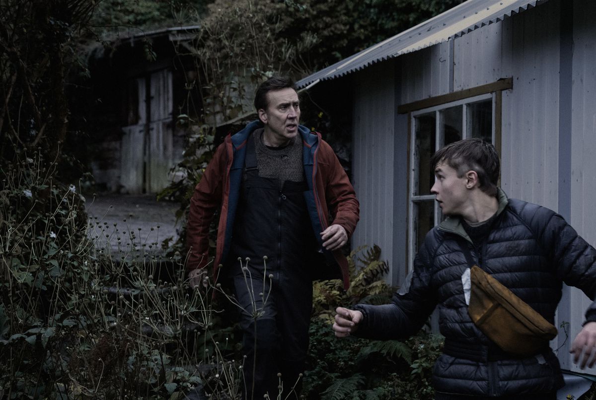 Nicolas Cage and Maxwell Jenkins walk outside a house through some plants in Arcadian.