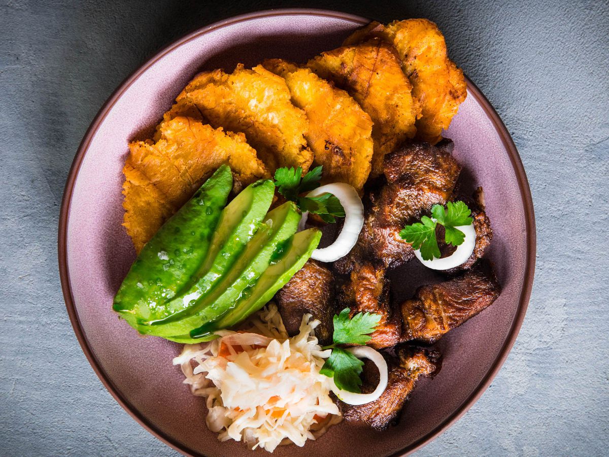 Fried plantains, avocado, pikliz, and more on a plate from Kann.
