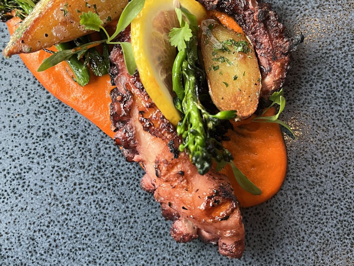 Large grilled octopus legs intertwined with roasted vegetables. 