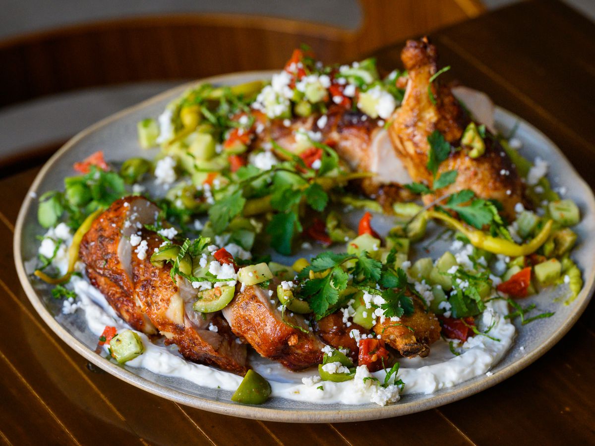A broken-down whole roasted chicken sits on a swab of green garlic labneh with a sprinkle of spring vegetables at Arden.