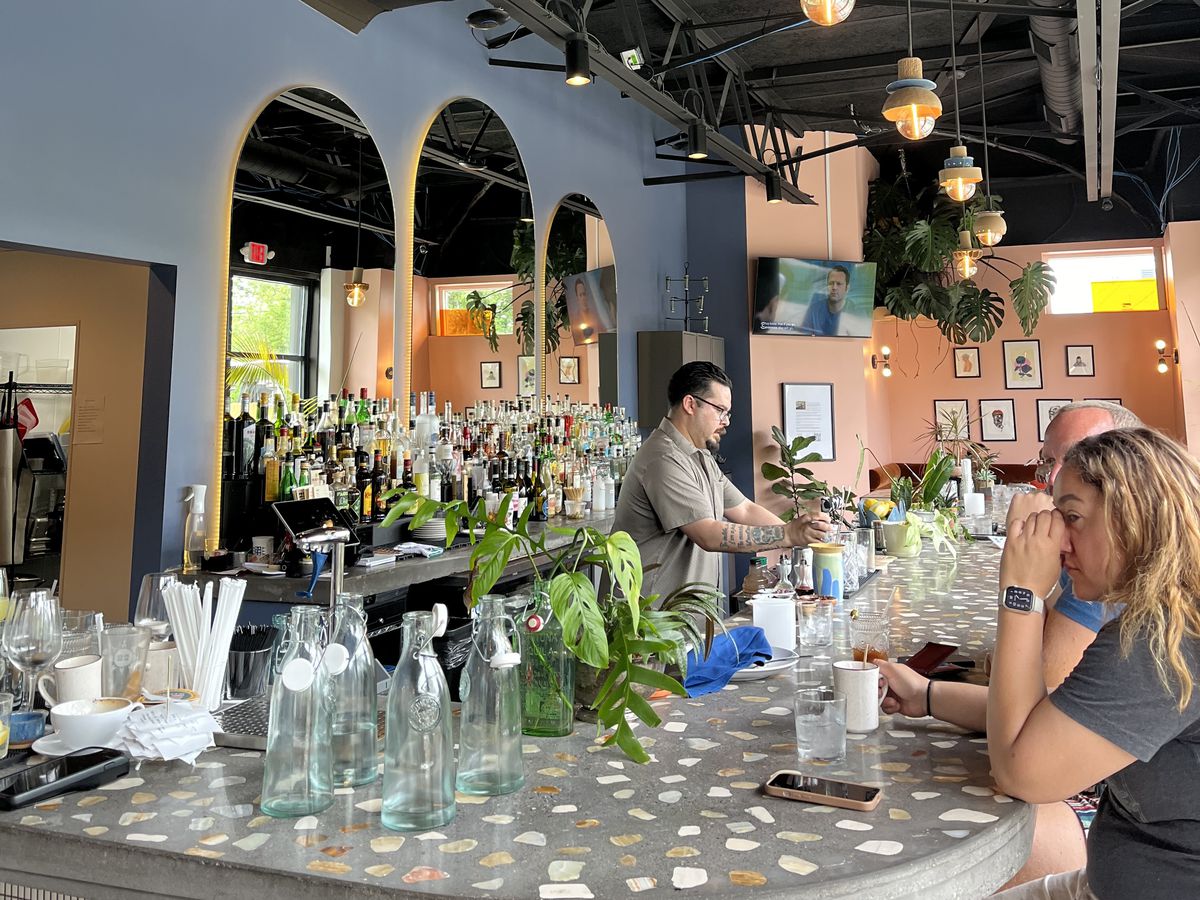 A bartender and customers at an airy, high-ceilinged bar.