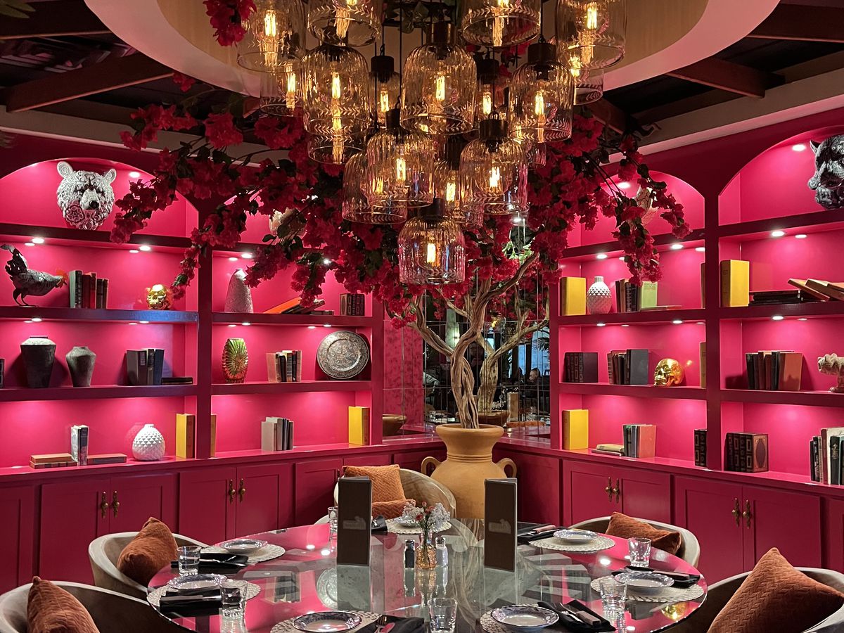 A bright pink dining area decorated with shelves, a large chandelier, and flowers. 
